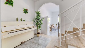 A modern interior with a piano, a staircase, and a dining area.