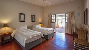 Habitación de hotel con dos camas, ventilador de techo, ventana con cortinas y vistas al exterior.