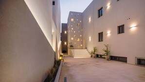 A narrow, well-lit corridor with a staircase leading to an upper floor, flanked by buildings with modern architecture and exterior lighting. - CELINE LUXURY APARTMENTS & SUITES (Agios Nikolaos)