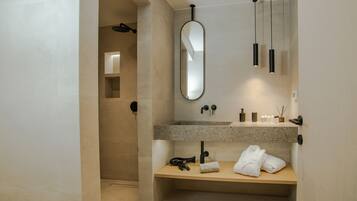 A modern bathroom with a granite countertop, a large mirror, a towel rack, and a shower area.