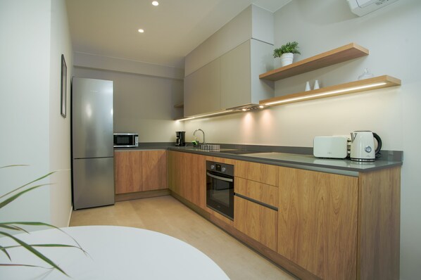 A modern kitchen with wooden cabinets, stainless steel appliances, and built-in shelves. - CELINE LUXURY APARTMENTS & SUITES (Agios Nikolaos)