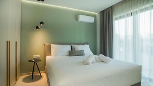 A neatly made bed with white linens and a folded towel, a bedside table with a remote control, and a wall-mounted air conditioner. - CELINE LUXURY APARTMENTS & SUITES (Agios Nikolaos)