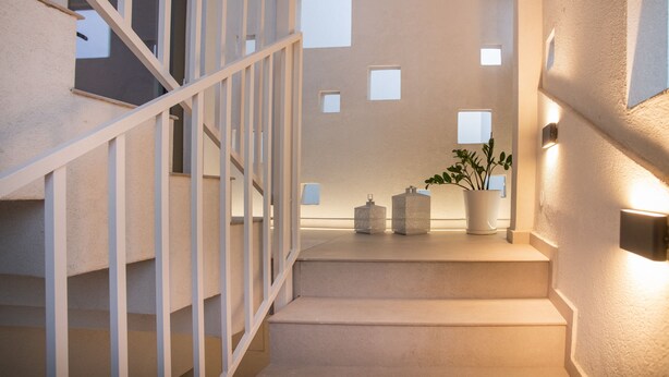 A modern staircase with a railing, a wall with square cutouts, and a potted plant. - CELINE LUXURY APARTMENTS & SUITES (Agios Nikolaos)