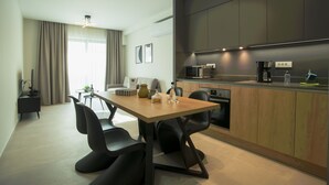 A modern kitchen with dark cabinetry, a wooden dining table, and black chairs. - CELINE LUXURY APARTMENTS & SUITES (Agios Nikolaos)