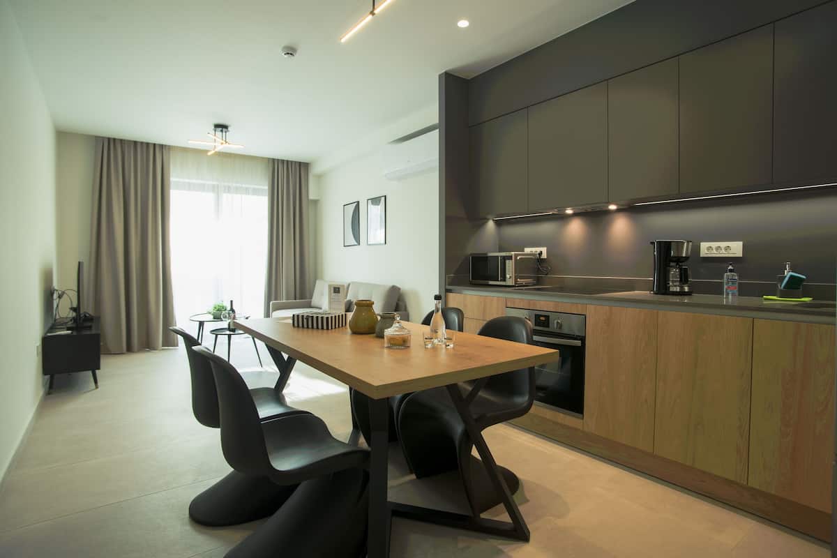 A modern kitchen with dark cabinetry, a wooden dining table, and black chairs.