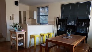 Eine moderne Küche mit Holzboden, einer zentralen Kochinsel mit Hockern, einem Kühlschrank und einem Fenster mit Jalousien.