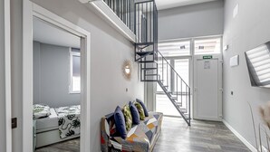 Ein modernes Interieur mit einer Treppe, einer Couch mit Kissen, einem Bett mit gemustertem Überwurf und einem an der Wand befestigten Spiegel.