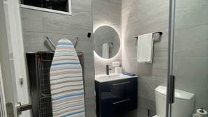 Une salle de bain moderne équipée d’une douche, d’un lavabo, de toilettes, d’un miroir et d’une planche à repasser.