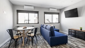 A modern living room with a sofa, dining table, chairs, and a TV mounted on the wall. - Modern near Santiago Bernabéu - AZCA Apartment (Madrid)