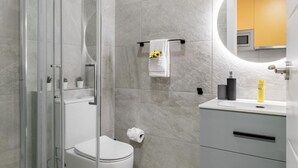 A modern bathroom with a glass shower enclosure, a toilet, a sink with a mirror, and a towel rack with a towel. - Modern near Santiago Bernabéu - AZCA Apartment (Madrid)