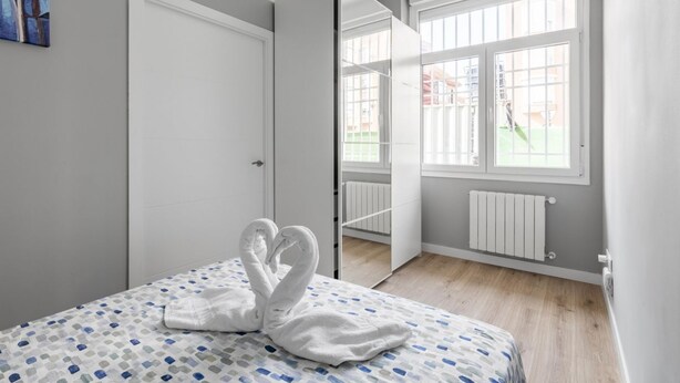 Une chambre à coucher avec un lit, une porte blanche, une fenêtre donnant sur un paysage et un radiateur.