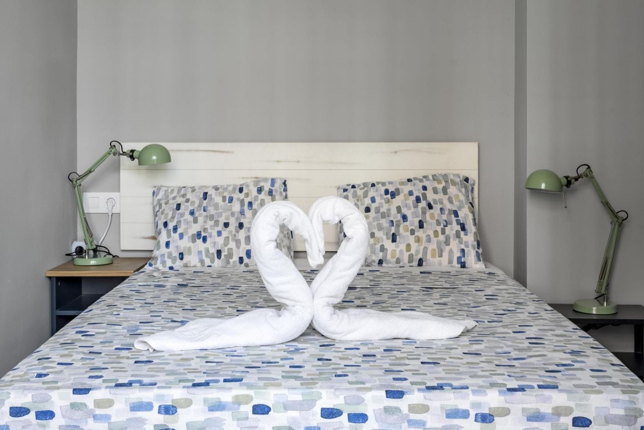 A bed with a geometric patterned bedspread, two bedside lamps, and pillows with a mosaic design.