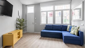Un salon moderne avec un canapé bleu, un meuble jaune, un téléviseur à écran plat et de grandes fenêtres.