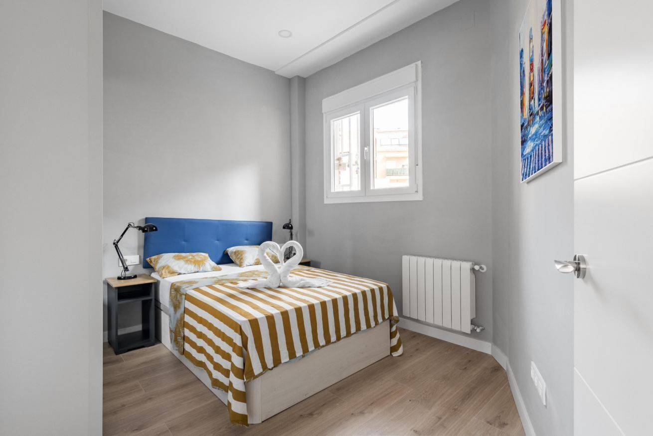 Un dormitorio con cama, mesita de noche, lámpara, ventana, radiador y una obra de arte en la pared.