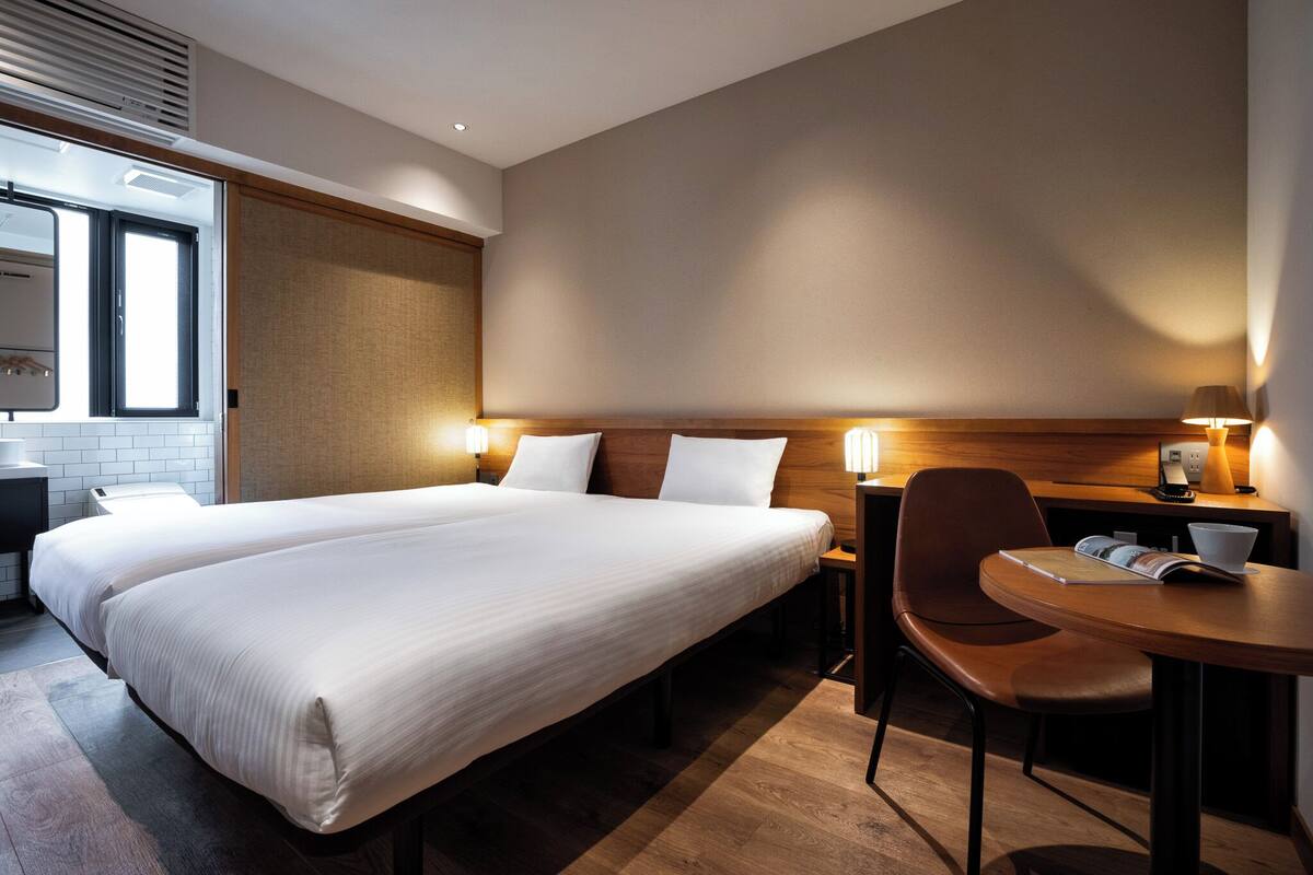 A hotel room with a large bed, bedside tables, a desk with a chair, and a window.