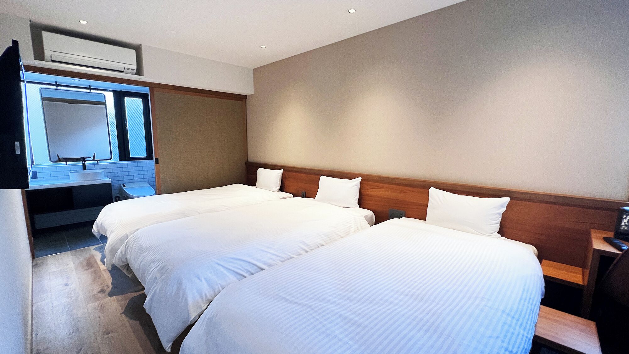 A hotel room with two beds, a bathroom with a sink and mirror, and a wooden headboard.