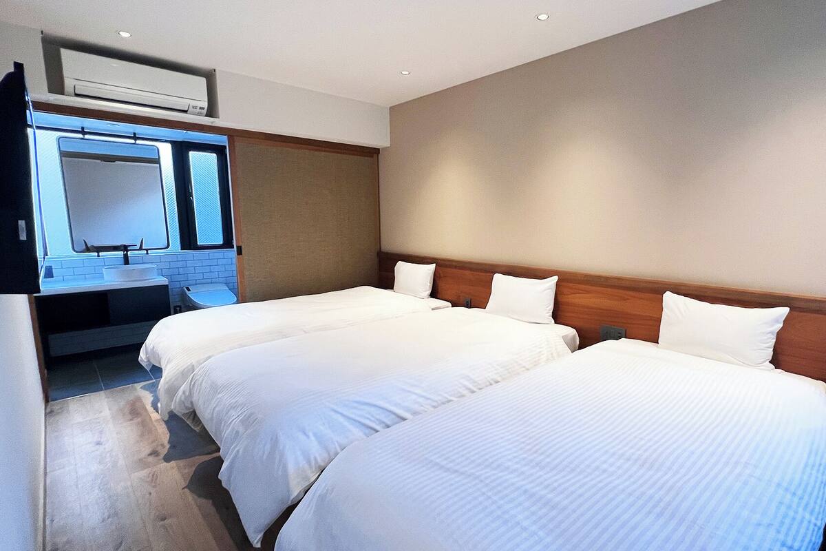 A hotel room with two beds, a bathroom with a sink and mirror, and a wooden headboard.