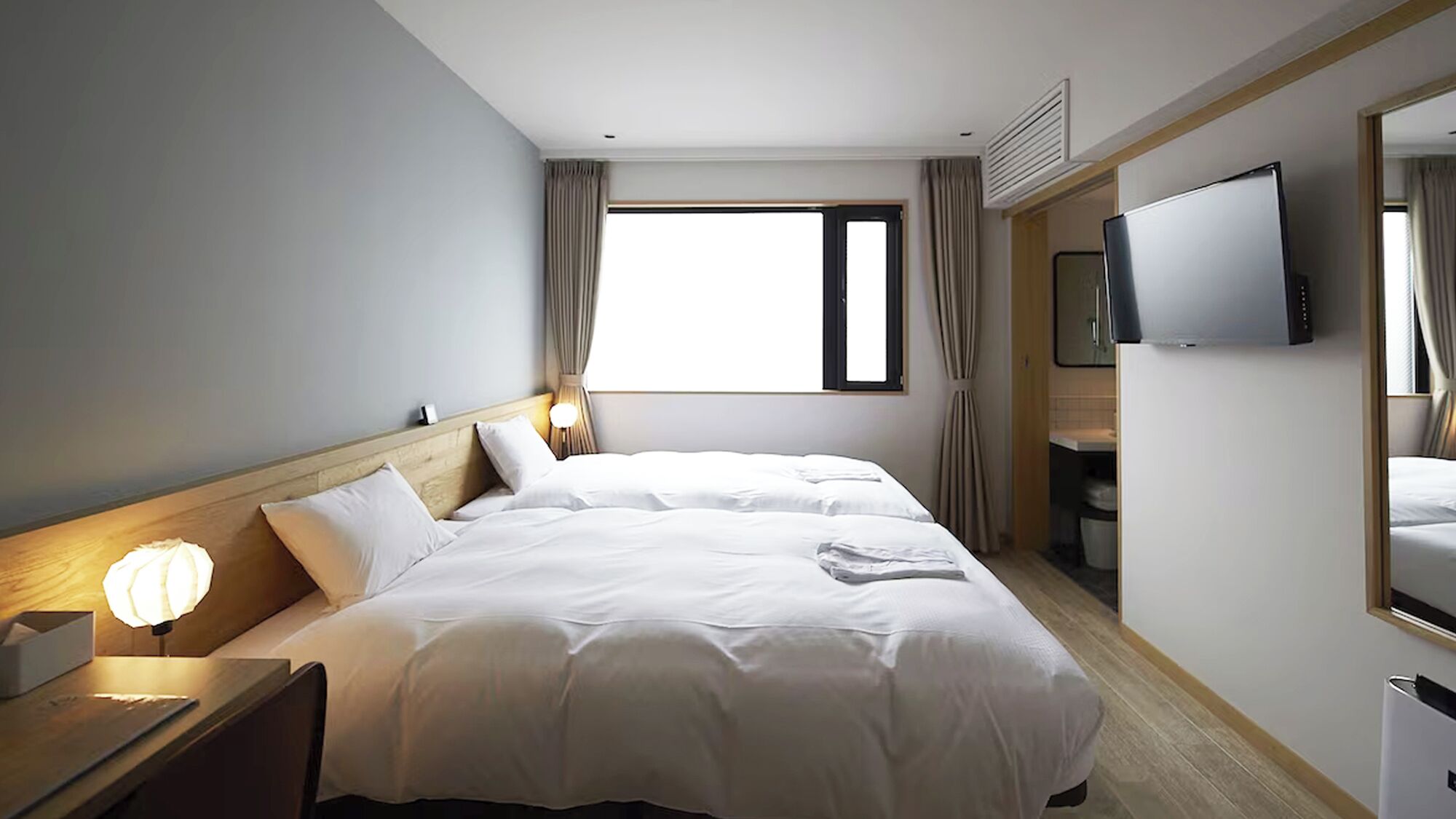 A hotel room with a bed, a bedside lamp, a TV, and a window with curtains.
