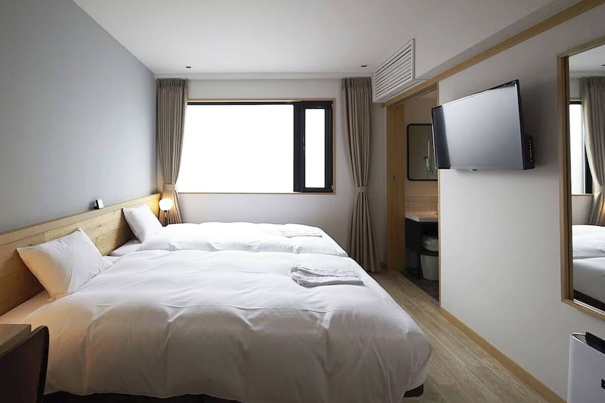 A hotel room with a bed, a bedside lamp, a TV, and a window with curtains.