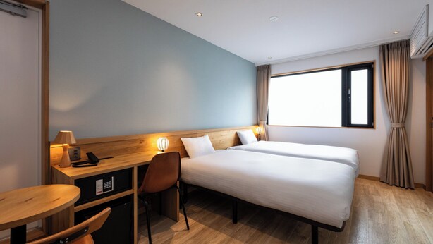 Ein Hotelzimmer mit Bett, Schreibtisch, Stuhl und einem Fenster mit Vorhängen.