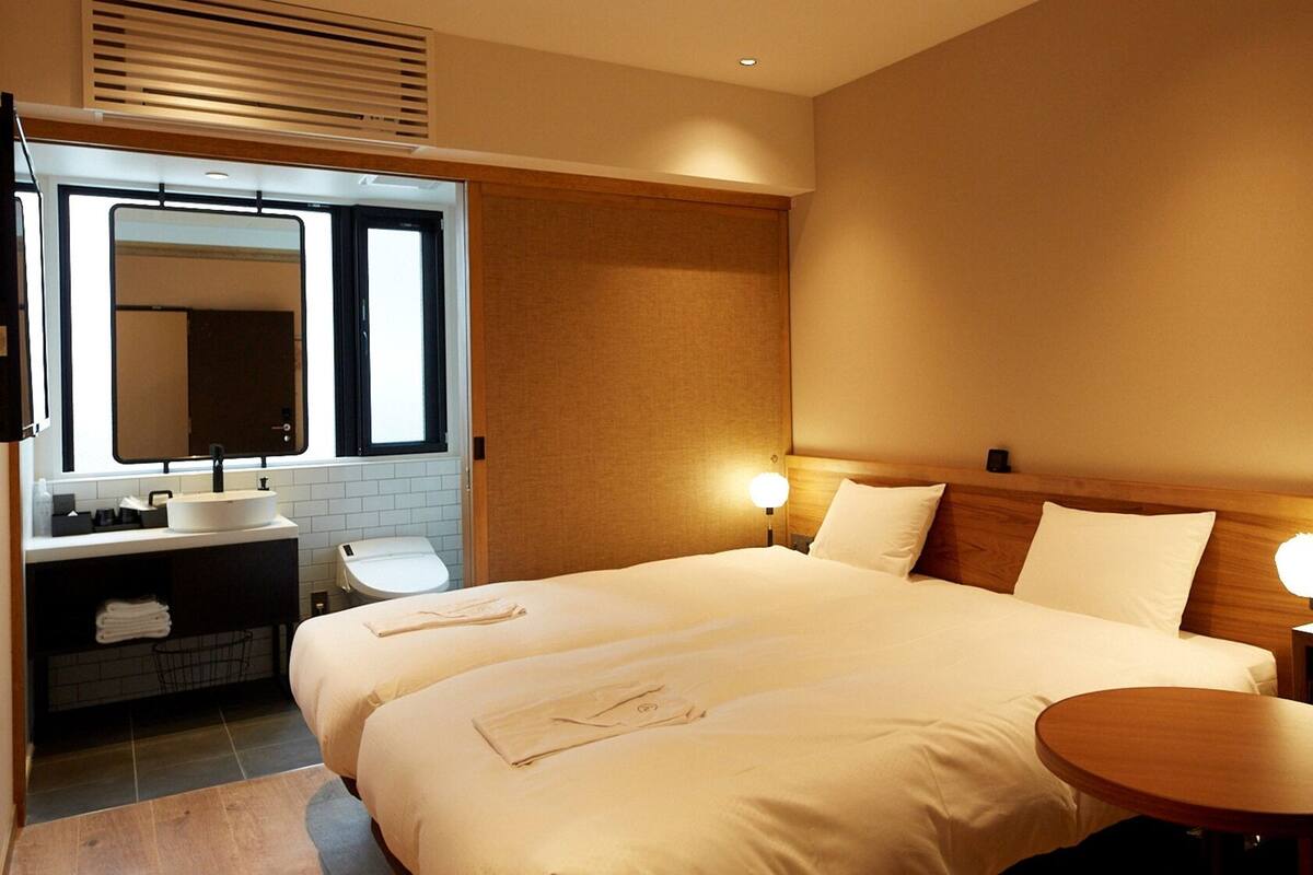 A hotel room with a double bed, a bedside table, a round table, a sink, and a mirror.