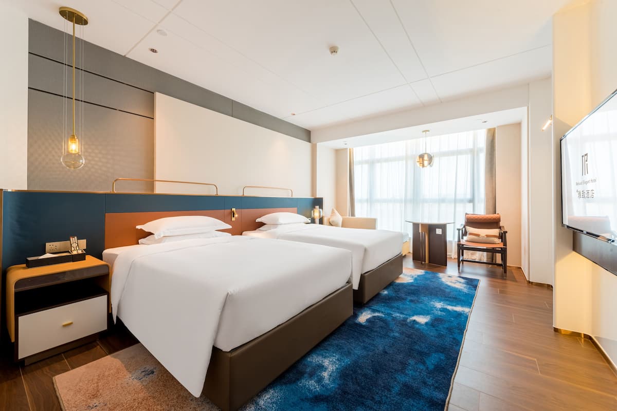 A hotel room with two beds, a desk, a chair, and a TV.
