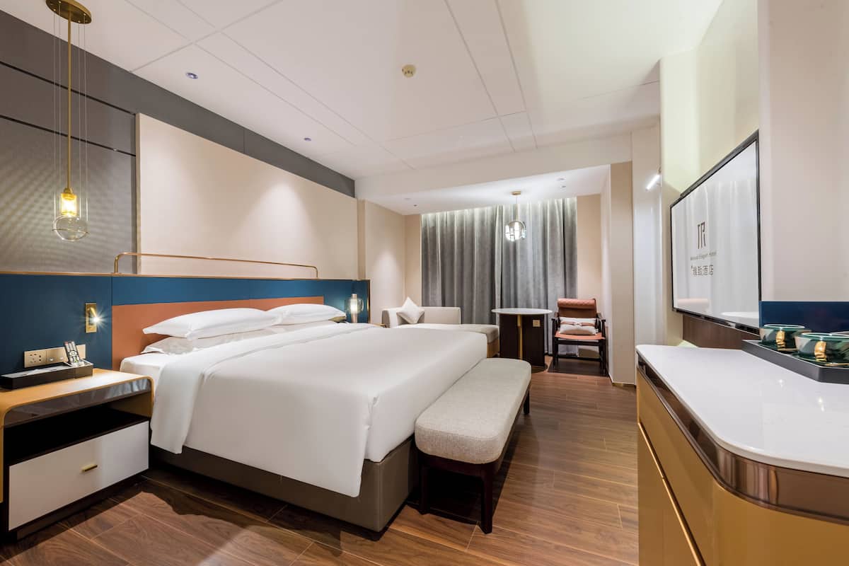 A modern hotel room with a large bed, bedside tables, a bench, a desk, and a mirror.