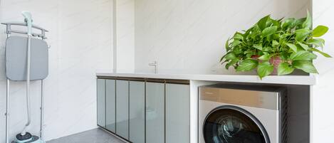 A modern laundry area with a washing machine, a vacuum cleaner, and a potted plant.