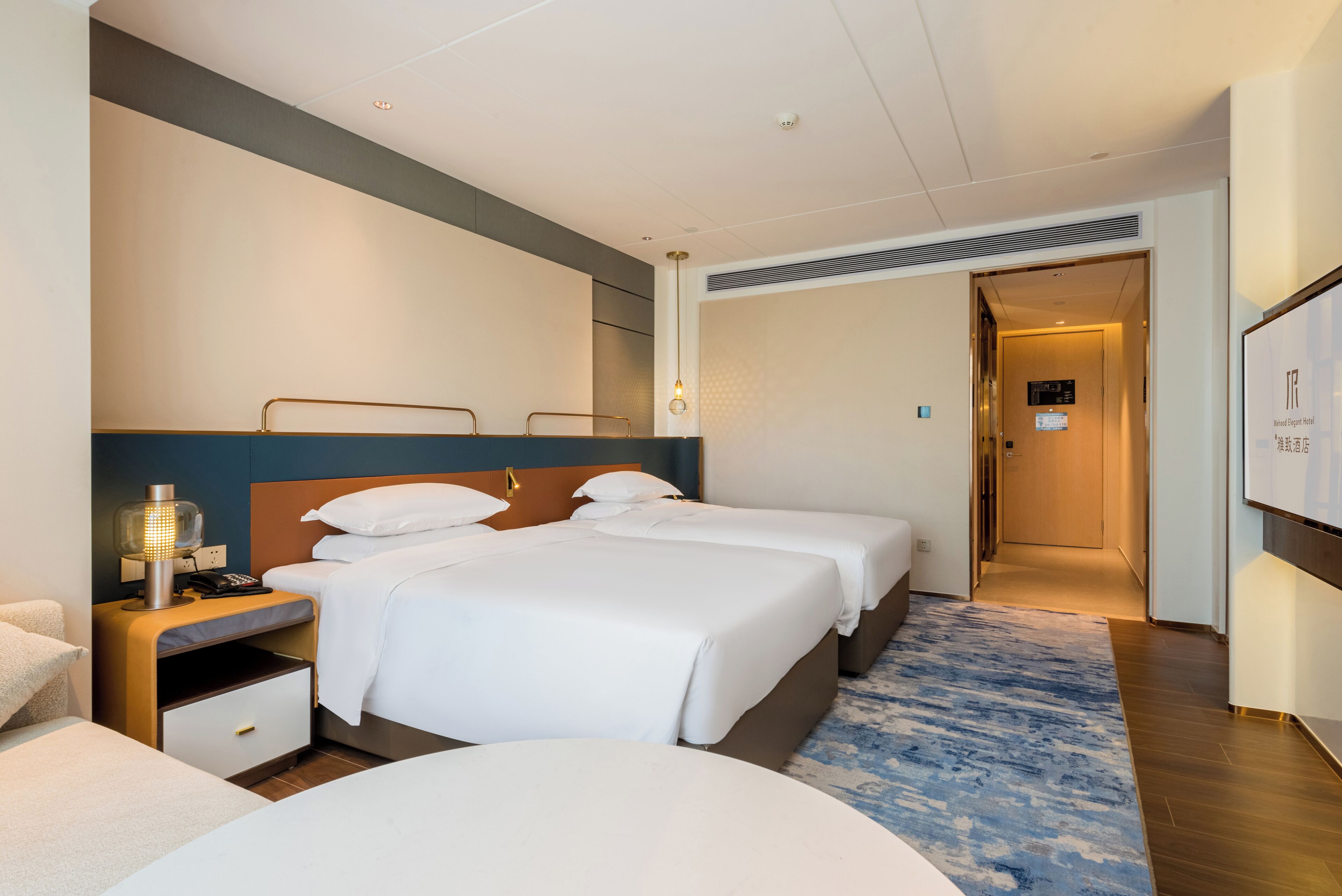 Une chambre d’hôtel avec deux lits, une table de chevet avec une lampe, un téléviseur fixé au mur et une porte de salle de bain.