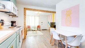Una cocina moderna con encimera de madera, cafetera y zona de comedor con sillas blancas y una mesa.