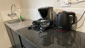 Een keuken met een granieten aanrecht, een koffiezetapparaat, een waterkoker en een spoelbak met een kraan.