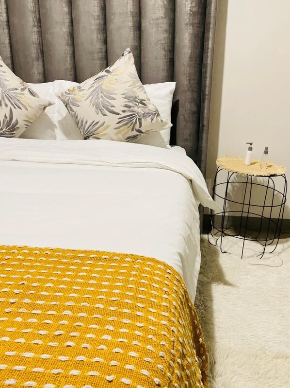 A bed with a white and yellow bedspread, grey curtains, and a small bedside table with toiletries. - Maboneng Modern Style (Johannesburg)