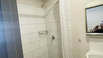 Ein kleiner Duschbereich mit Fliesen, ein weißes Waschbecken und ein Spiegel darüber.