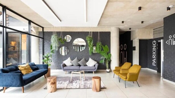 Een moderne lobby met een blauwe bank, een grijze bank, gele stoelen en een grote spiegelwand.