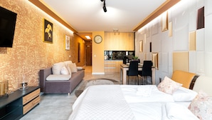 A modern hotel room with a sofa, a bed, a dining area, and a kitchen in the background. - Apartamenty Sun & Snow Green Park (Szklarska Poreba)