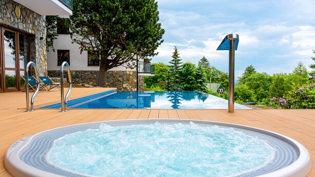 A swimming pool with a hot tub, lounge chairs, and a stone wall. - Apartamenty Sun & Snow Green Park (Szklarska Poreba)