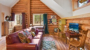 A cozy log cabin interior with a leather sofa, wooden furniture, a television, and a scenic view through the windows. - Carnelian Lodge Log Cabin, Sleeps 9, Hot Tub (Carnelian Bay)
