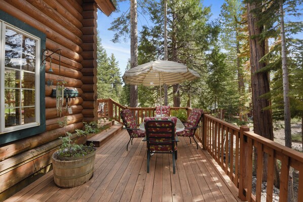 Une terrasse en bois, agrémentée d’une table et de chaises, entourée d’une balustrade en bois, située dans un espace boisé.