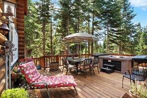 A wooden deck with a grill, outdoor seating, and a view of tall trees. - Carnelian Lodge Log Cabin, Sleeps 9, Hot Tub (Carnelian Bay)