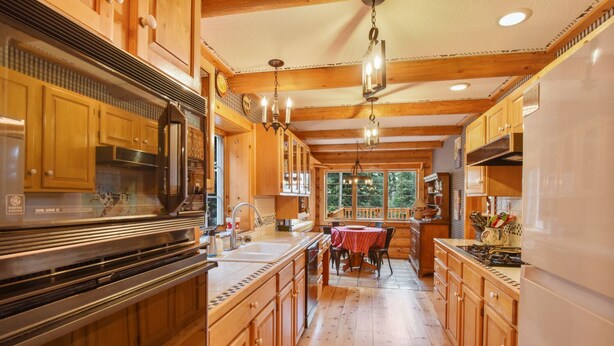 A spacious kitchen with wooden cabinets, a central island, and a dining area with a table and chairs. - Carnelian Lodge Log Cabin, Sleeps 9, Hot Tub (Carnelian Bay)