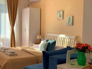 A hotel room with a bed, a wardrobe, a nightstand, a lamp, a vase with flowers, and two wall art pieces. - The Rooftop Apartment with Sea view (Ulcinj)