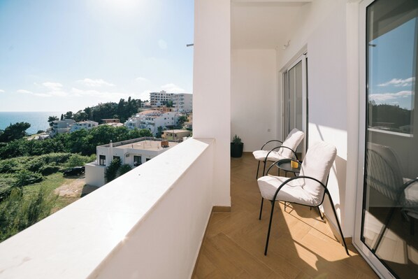 A balcony with a view of the sea and buildings, white walls, and two white chairs. - The Rooftop Apartment with Sea view (Ulcinj)