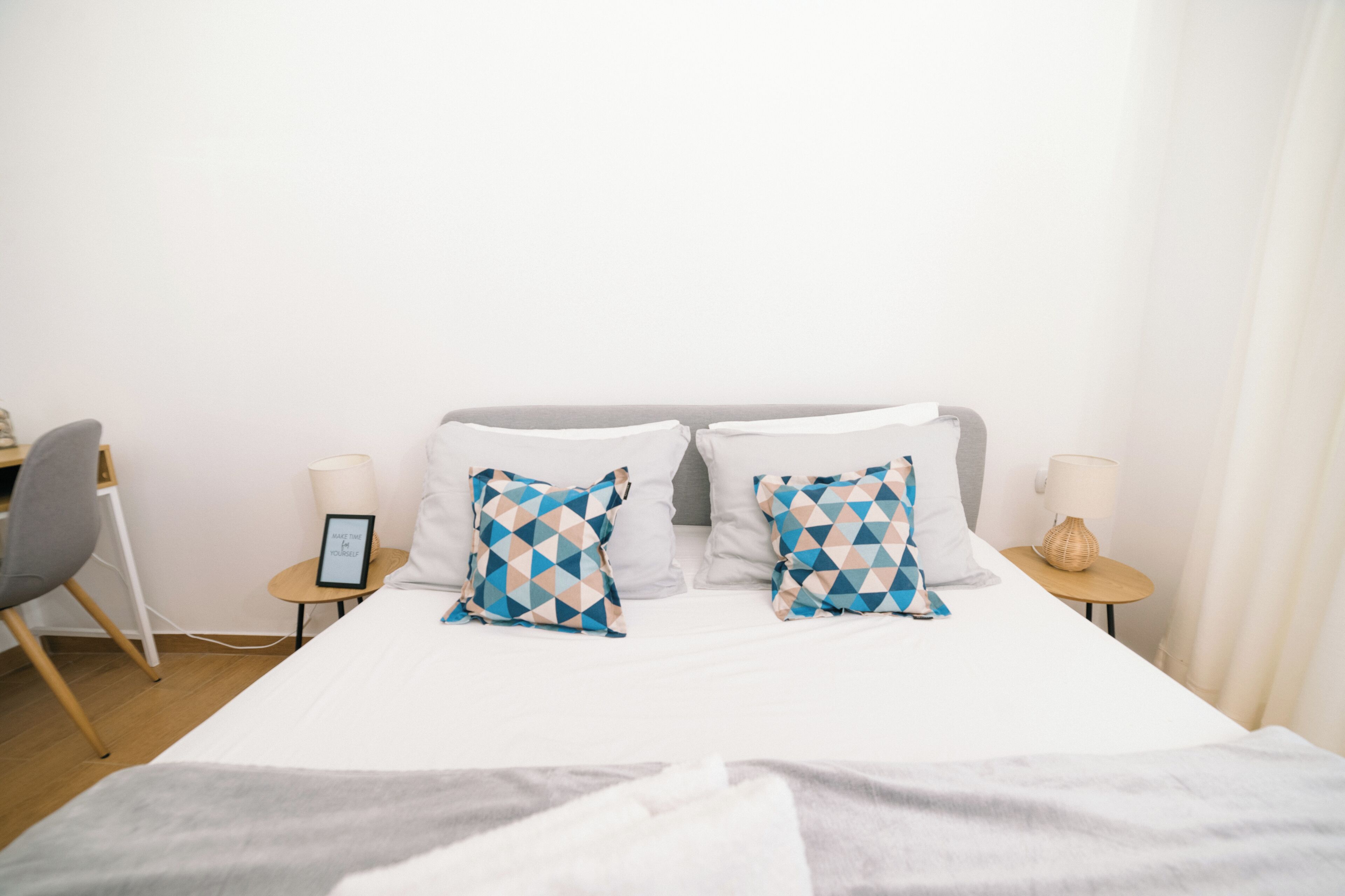 A neatly made bed with two patterned pillows, a bedside table with a lamp, and a chair.
