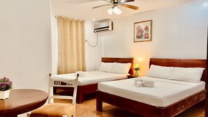 A hotel room with two single beds, a wooden table with a chair, an air conditioning unit, and a ceiling fan. - Tagzzz Hotel powered by Cocotel (Tagaytay)