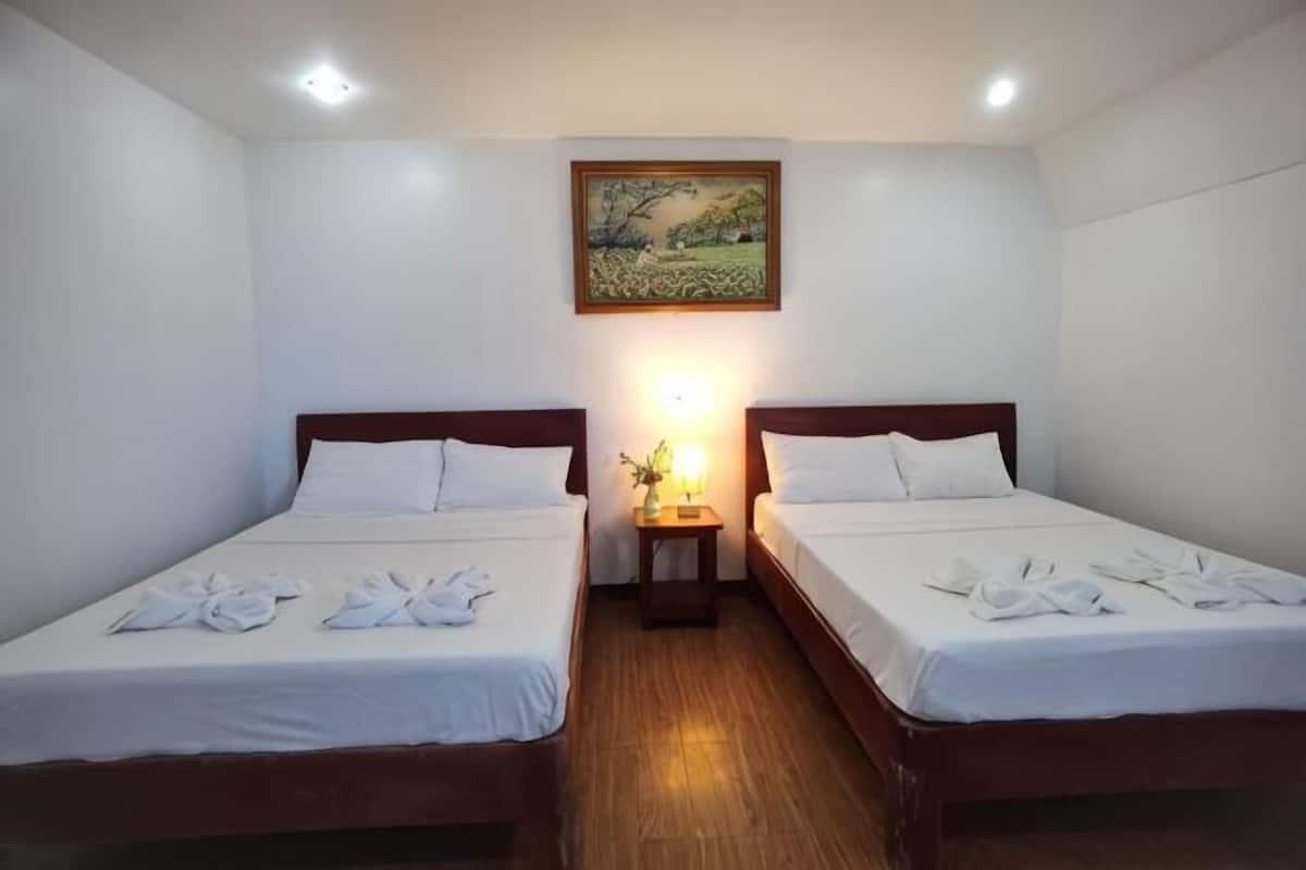 Une chambre avec deux lits, un tableau au mur et une table de chevet avec une lampe.