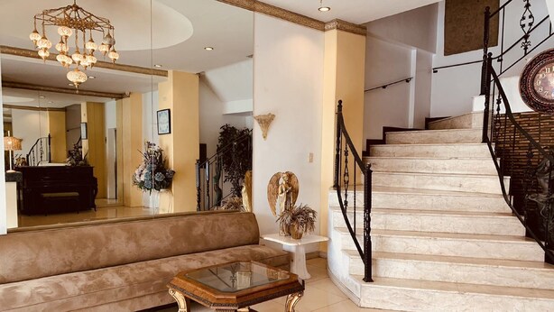 A spacious living area with a grand staircase, a sofa, a glass-top coffee table, and decorative elements like a chandelier and wall art. - Tagzzz Hotel powered by Cocotel (Tagaytay)