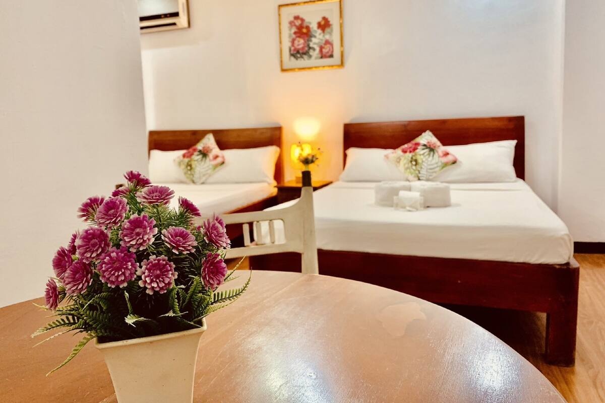 Une chambre d’hôtel avec deux lits, une table ornée d’un vase de fleurs et un tableau encadré accroché au mur.