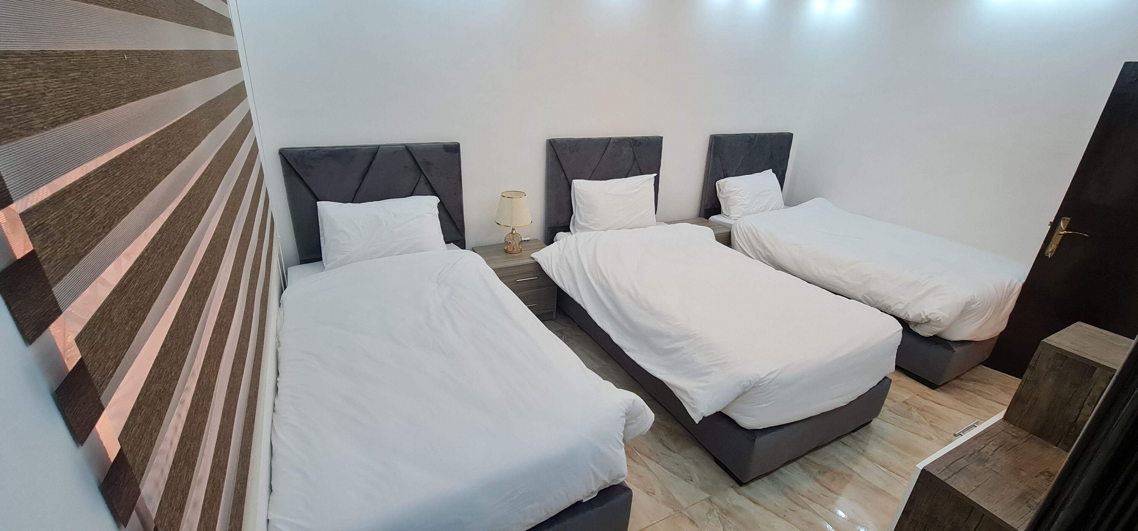 A hotel room with three single beds, a wooden floor, and a striped carpet.