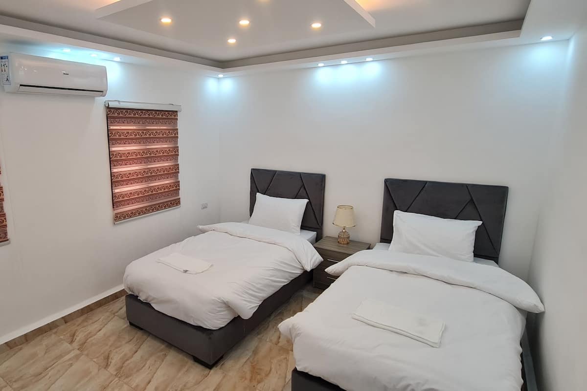 A modern hotel room with two beds, an air conditioning unit, patterned curtains, and a wooden floor.