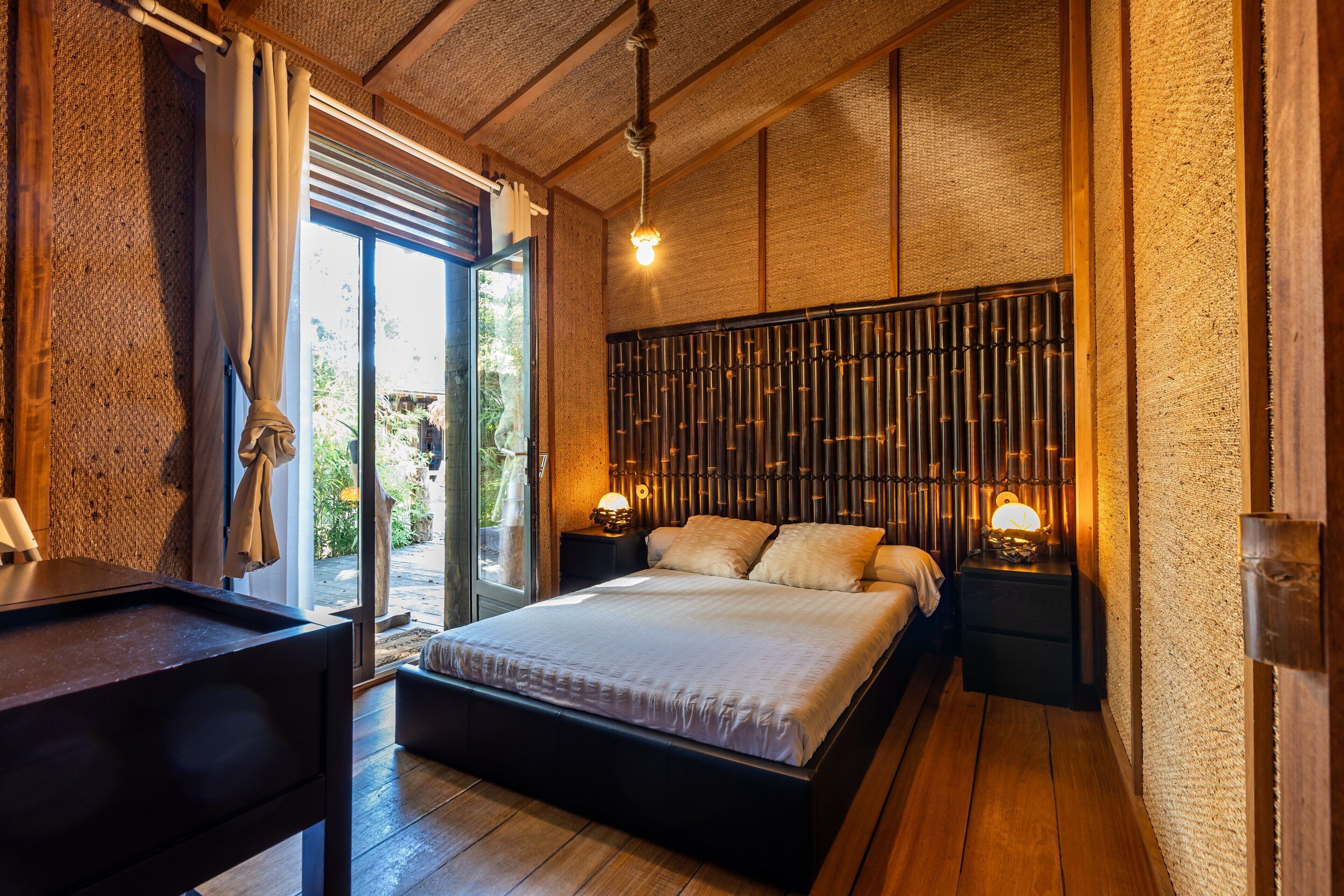 Un dormitorio con cama, mesitas de noche, una ventana y vistas al verde exterior.